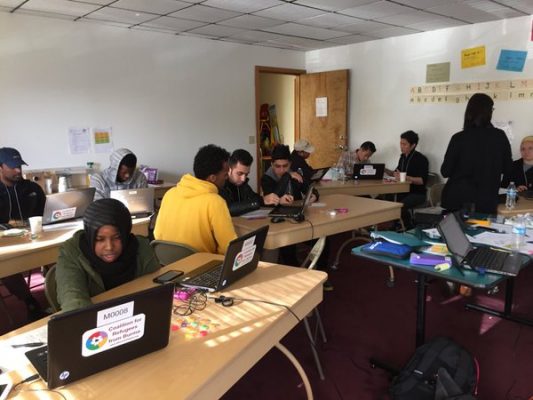 Volunteers and Burmese refugees working at laptop computers together.
