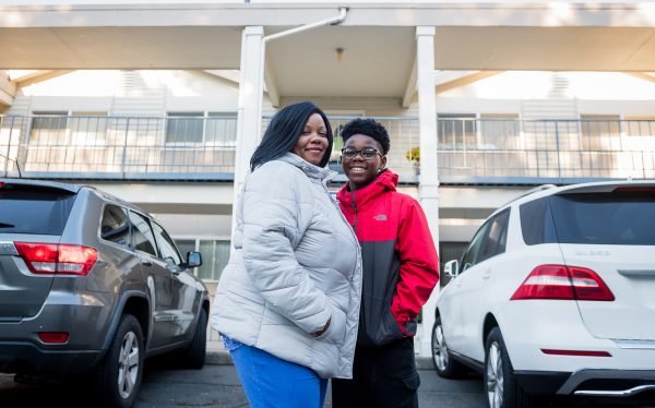 End homelessness with United Way of King County Streets to Home. Formerly homeless black woman smiling in front of new home with her teenage son