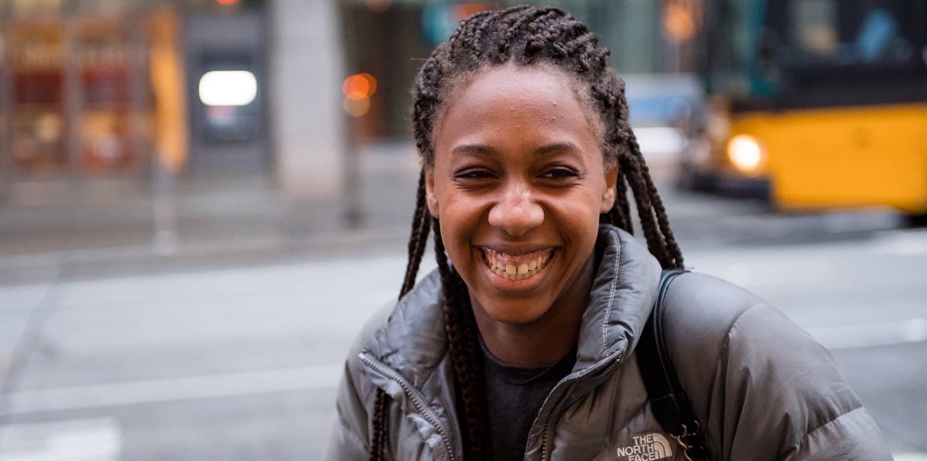 Photo of November, a smiling young woman Black woman standing on the sidewalk.