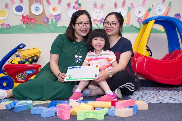 Mother, young daughter and home visitor in the Parent-Child Home Program smile with young girl's graduation certificate from the program.