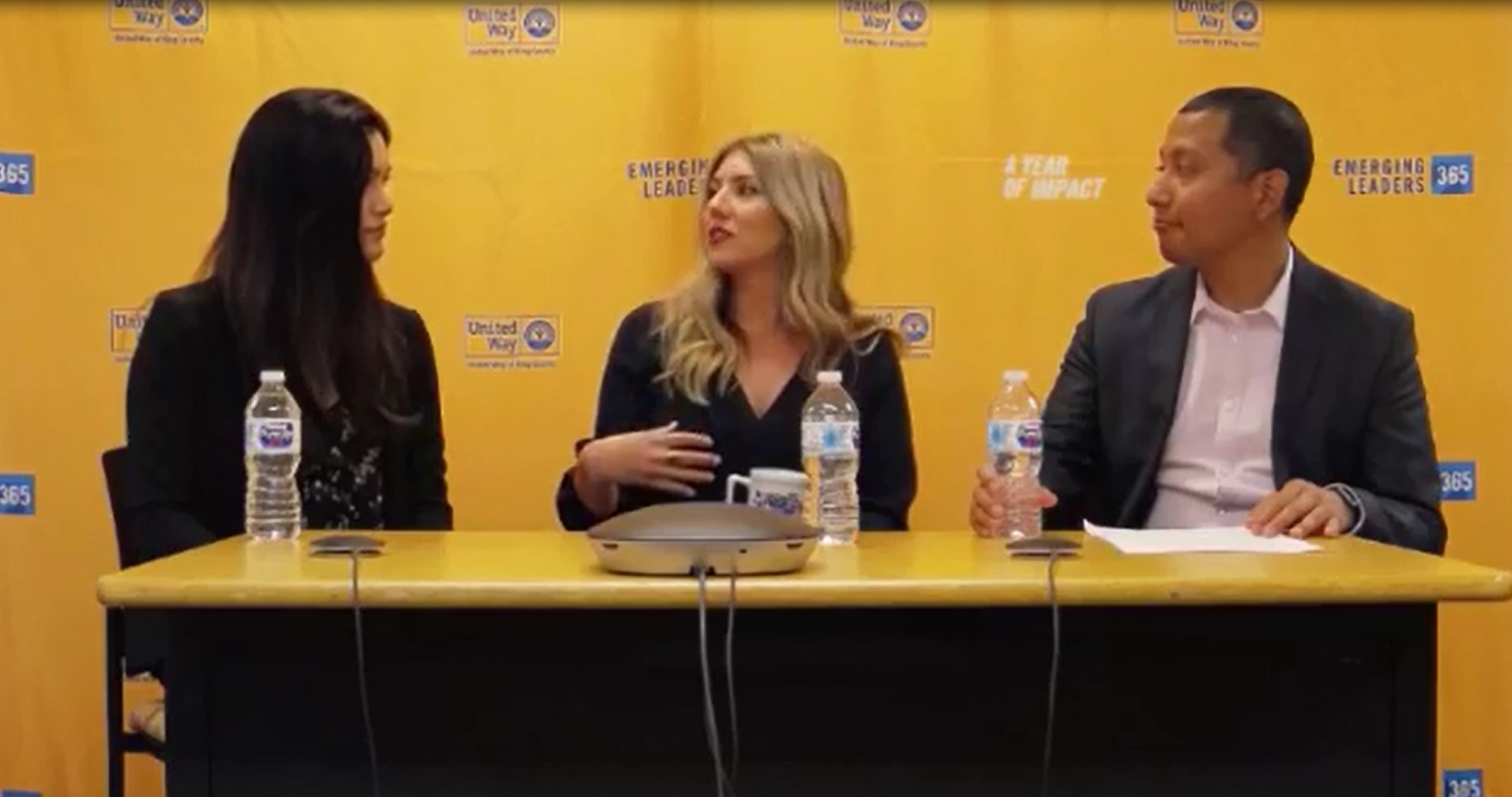 Image of the panelists sitting in front of a yellow background and talking