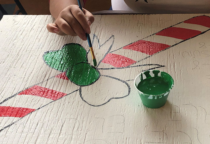 A person's hand paining a bow on a drawing of a candy cane.