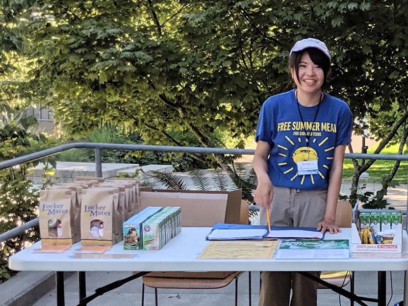 A free summer meals provider stands behind a table with free samples.