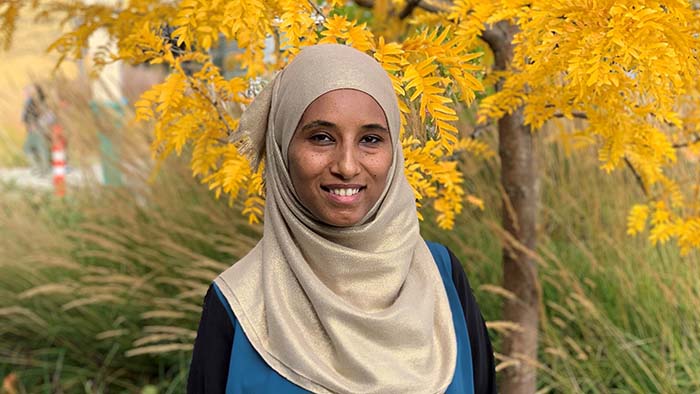 A woman wearing a headscarf, smiling and looking into the camera.