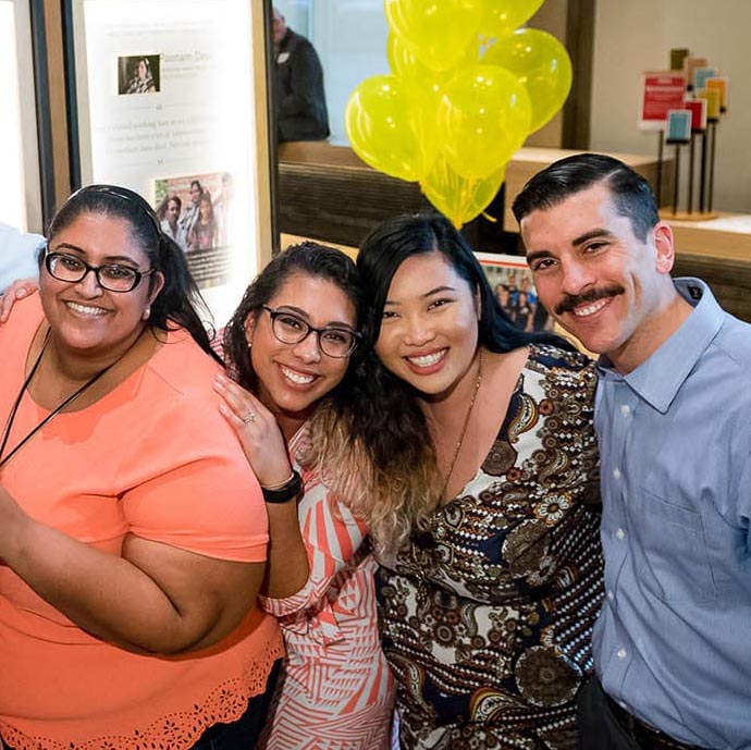 Group photo of four emerging leaders at an event with yellow balloons in background