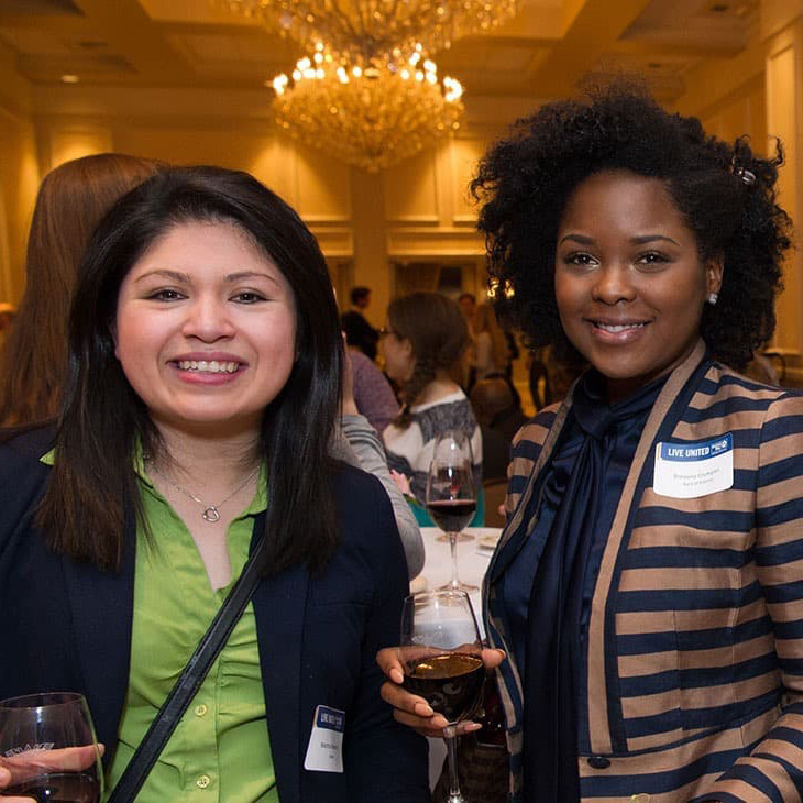 Two people standing and smiling holding wine glasses at an event