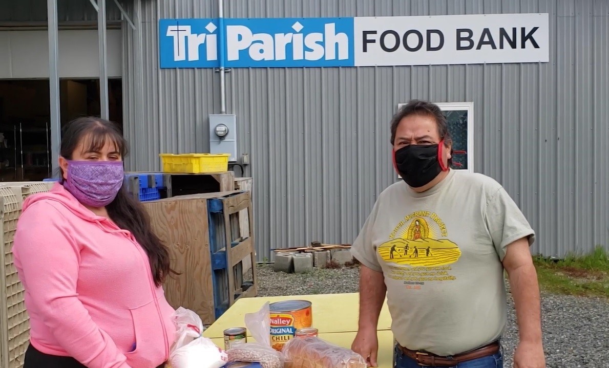 Two people wearing masks standing by a food bank table.