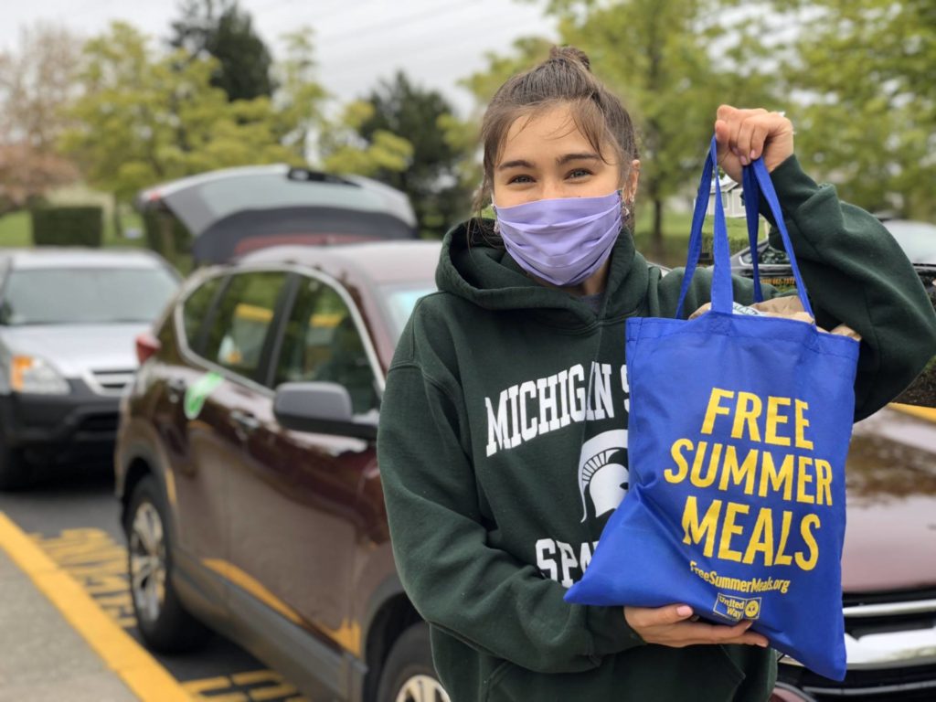 A woman wearing a mask and holding a free summer meals bag.