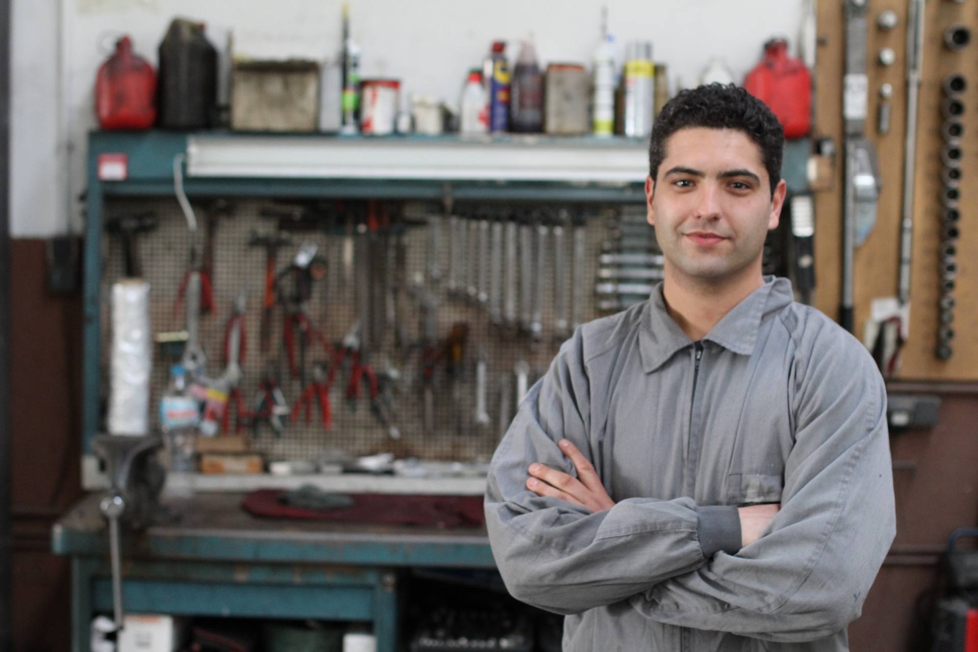 A man wearing overalls looking at the camera with a rack of tools behind him.