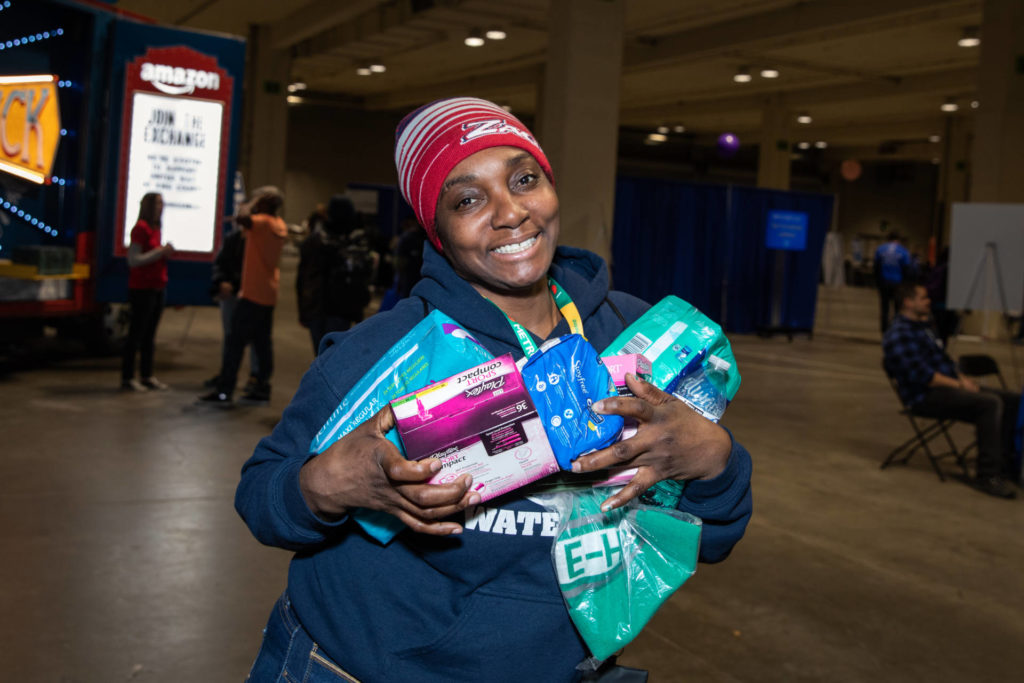 A Guest at the 2019 Community Resource Exchange stands smiling at camera holding supplies given at the event.