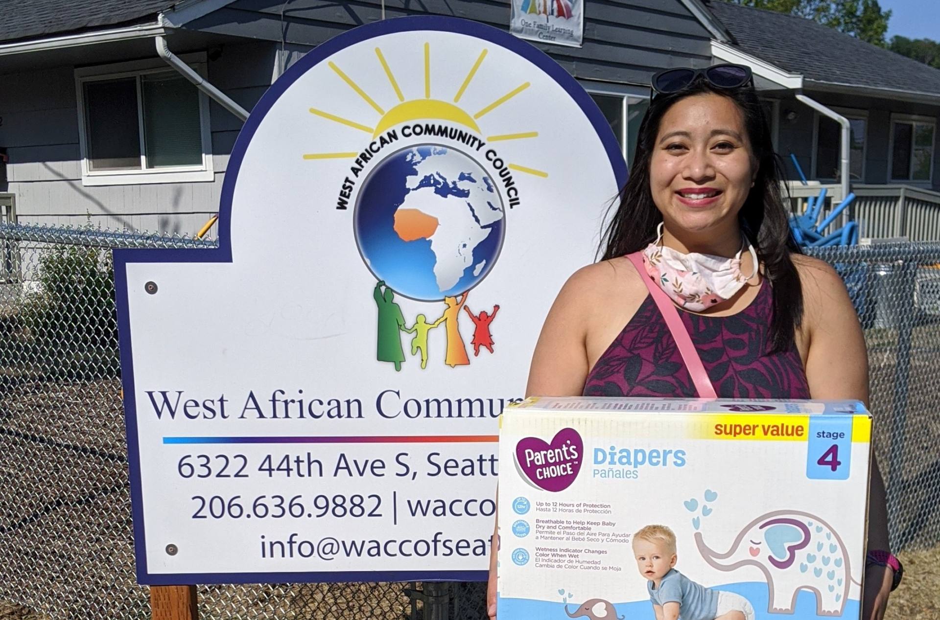 A woman standing outside a building holding a box of diapers.