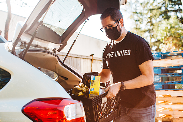 person wearing a Live United shirt loads a container of groceries into the trunk of a doordash car