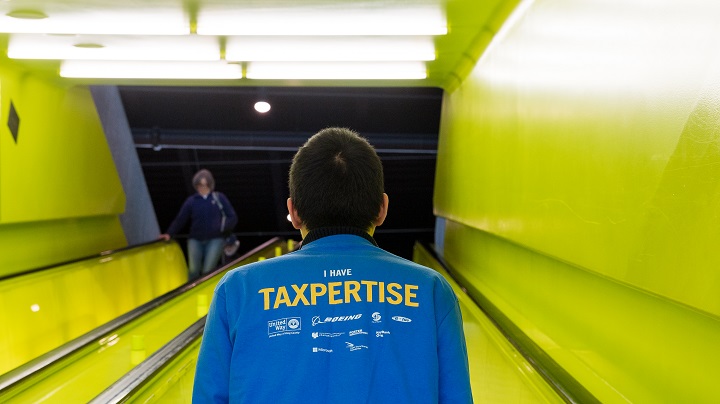 A person with his back toward the camera on an escalator. His shirt says 