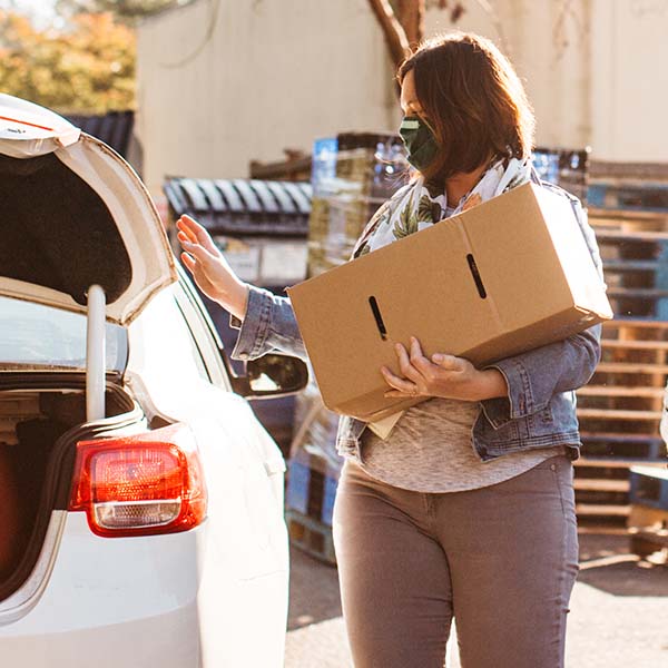 A person holding a box of food approaches a car with the trunk open