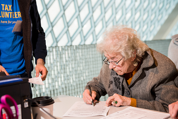 Elderly person with short curly hair fills out a tax form at a tax help site.