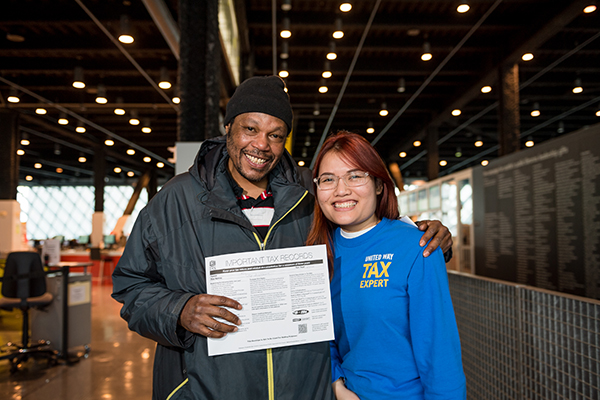 A tax volunteer poses with a person who holds up a tax document. both are smiling and looking at the camera.