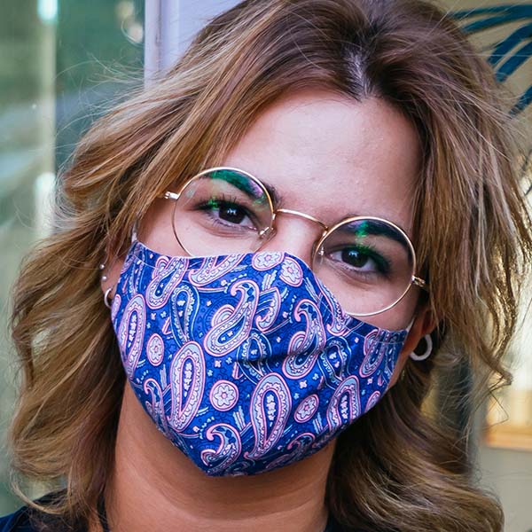 A teen with long wavy hair looks at the camera wearing glasses and a cloth face mask as a precaution during the covid-19 pandemic.