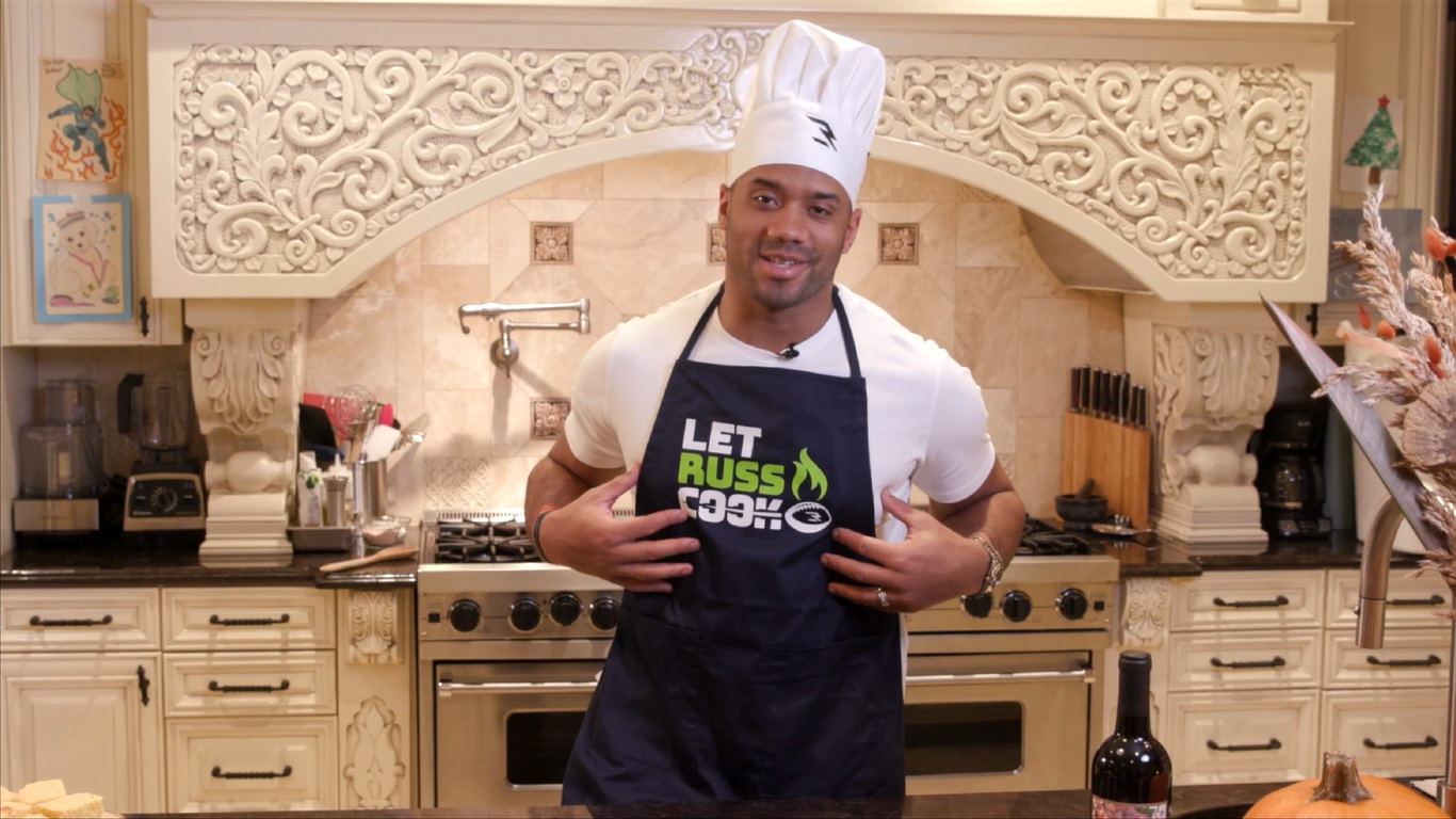 A man in a kitchen wearing a chef's hat and an apron.