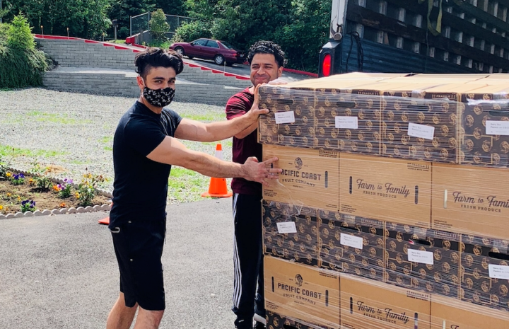 Two men, one wearing a mask, getting ready to unload boxes from a truck.