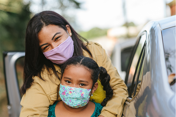 mother and daughter wearing masks and standing next to car