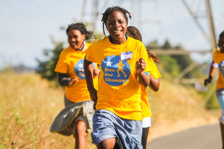 A group of Congolese youth running in the sun and smiling.