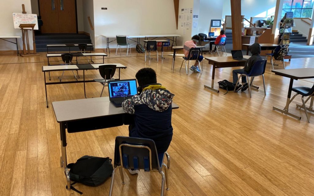 A couple of students sitting by computers during virtual classes. Social distance is maintained.