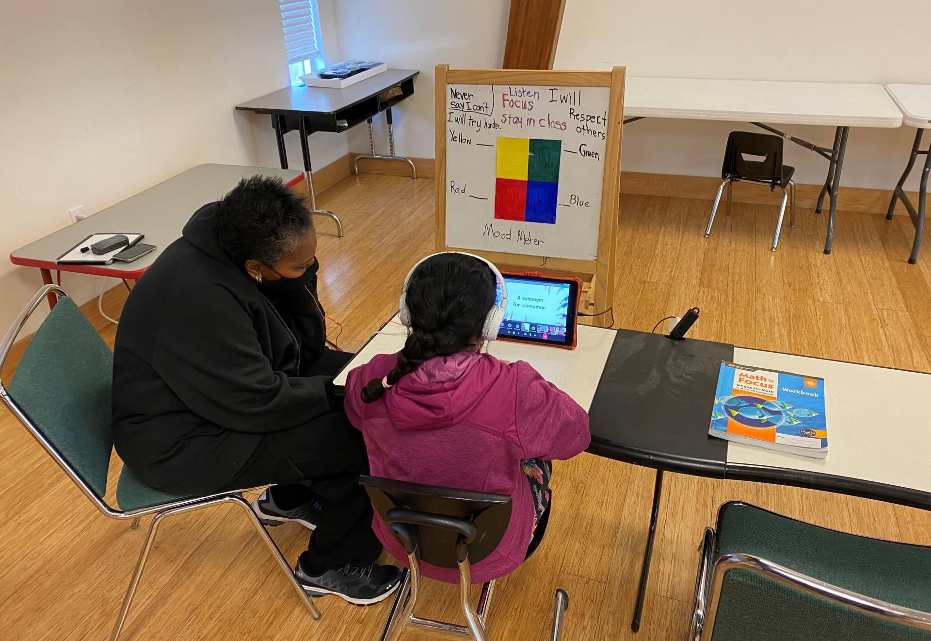 An adult sitting by a student who is learning virtually.