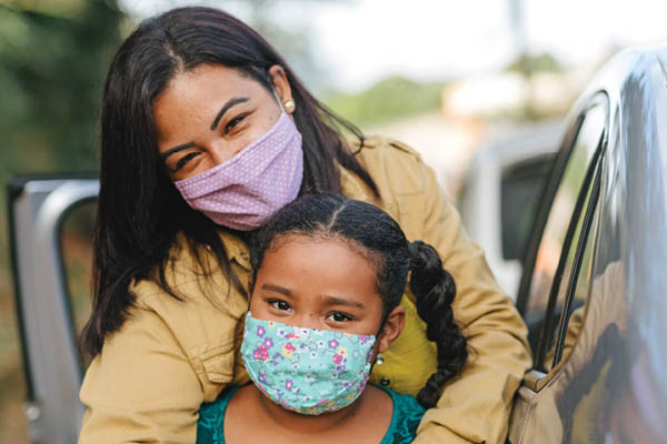A parent wearing a medical face mask embraces a child wearing a medical face mask