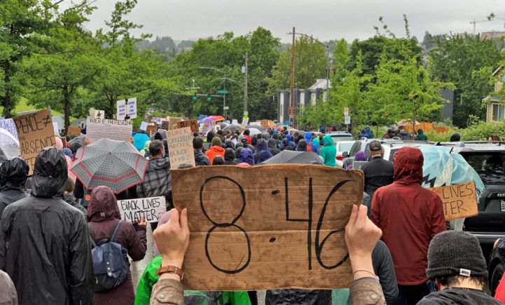 A large protest with a hand-made poster that says 8:46 in the foreground.