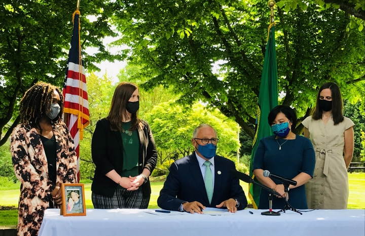 Governor Inslee sitting at a table signing the Working Families Tax Credit surrounded by supporters.