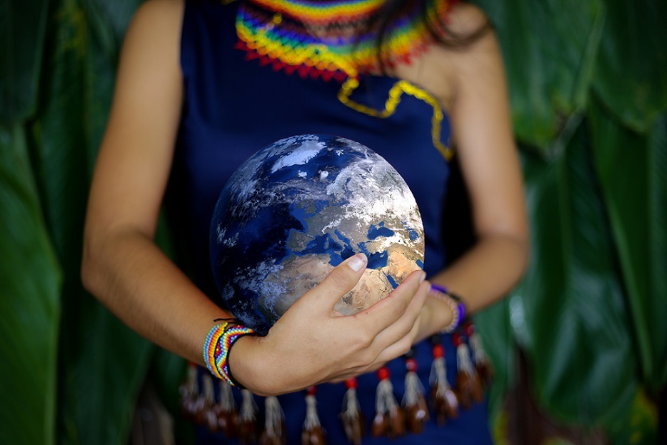 An Indigenous woman in traditional clothing holding the earth with two hands