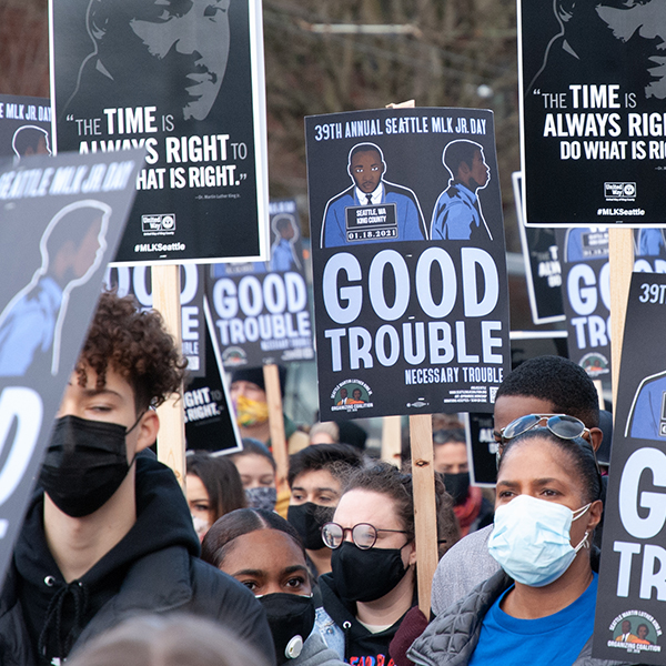 MLK Day rally with people in the march holding posters that say "Good Trouble"