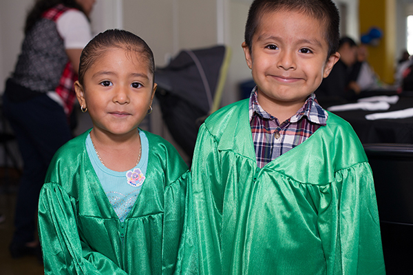 Two young children wear green graduation gowns and smile at the camera.
