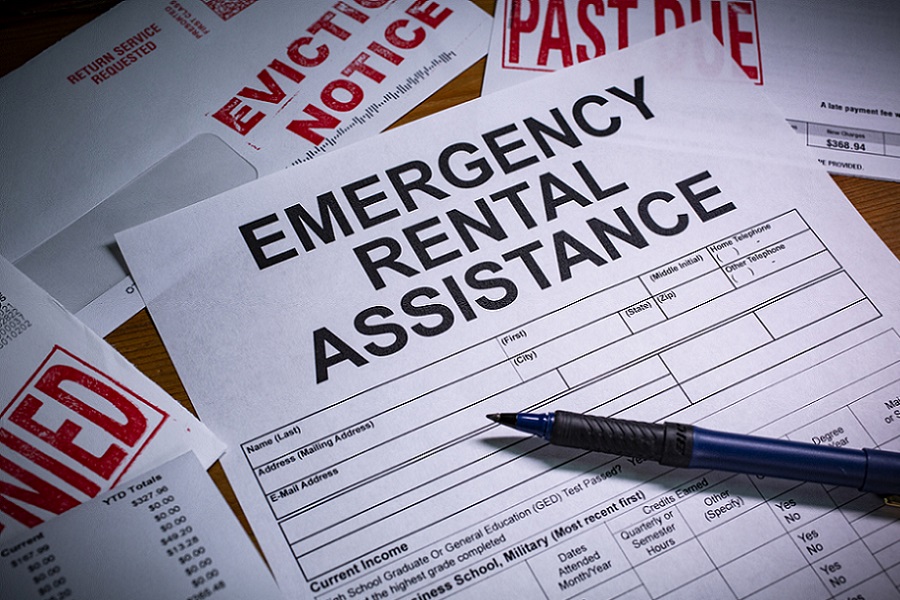 A blank application for Emergency Rental Assistance is on a desktop. An Eviction notice and Past Due paperwork is nearby.