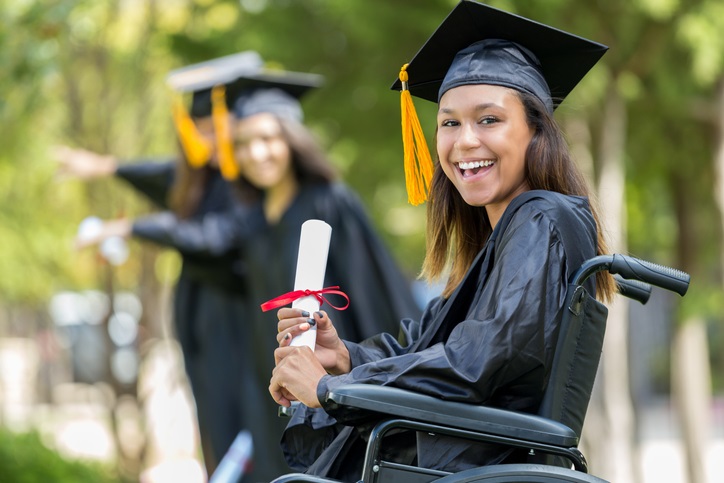 Beautiful African American female college graduate in wheelchair smiles confidently while holding her diploma.